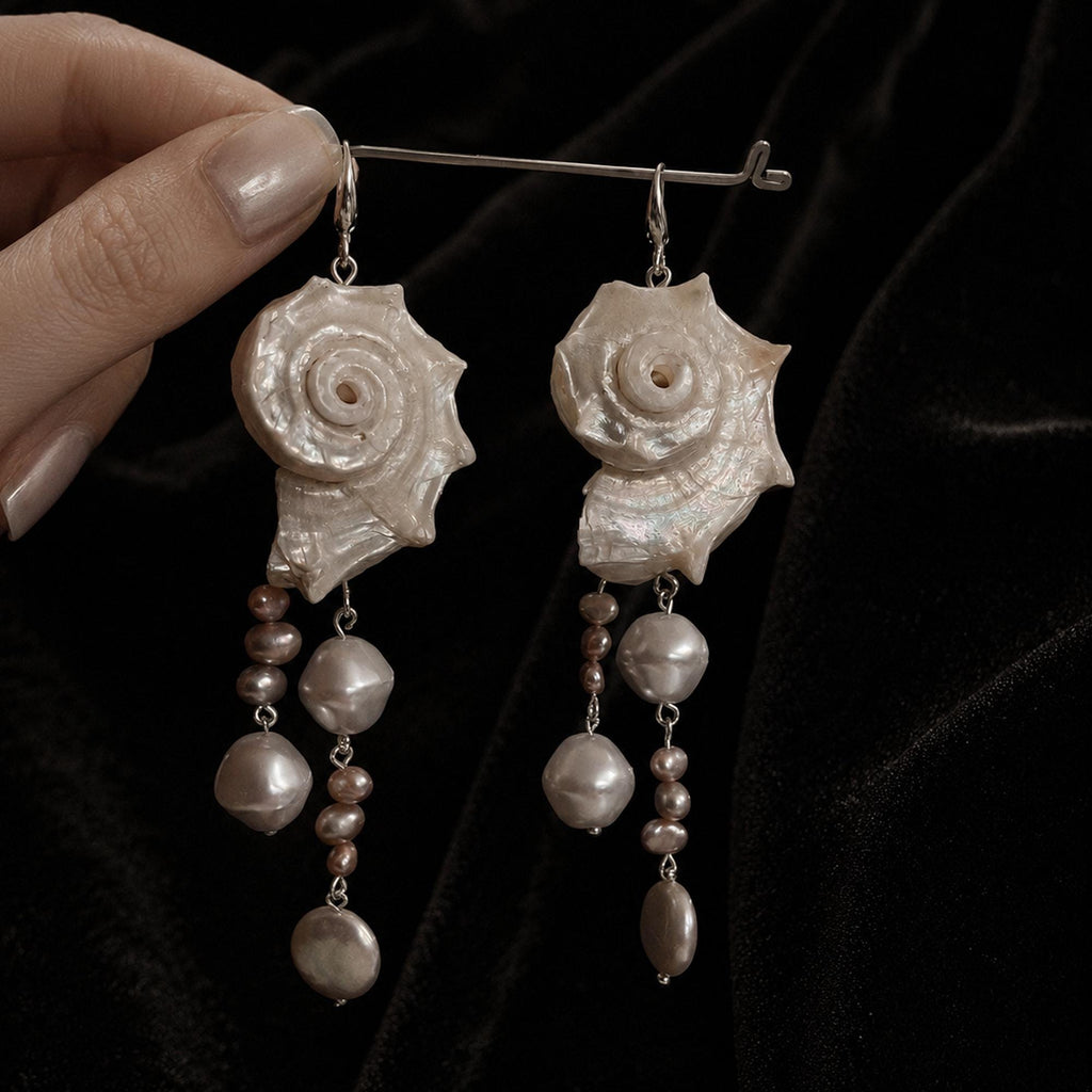 Pair of long conch-shell earrings with pale bead drops suspended from a metal bar.
