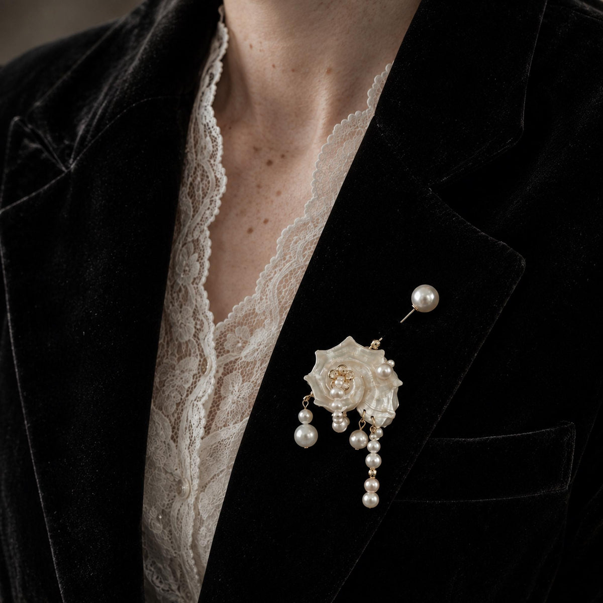 Conch-shell brooch with a long pearl-topped pin worn on a black blazer.