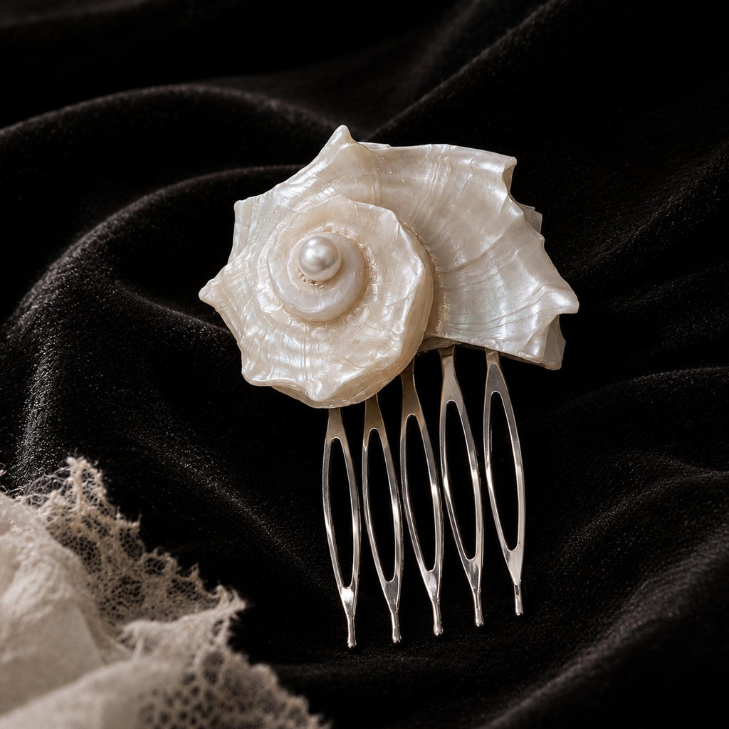Conch-shell hair comb resting on dark fabric with its metal teeth visible.