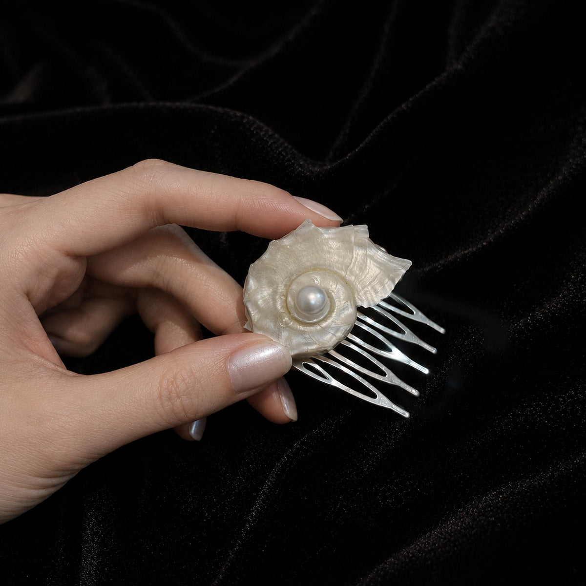 Conch-shell hair comb held in a hand to show its scale and curved teeth.