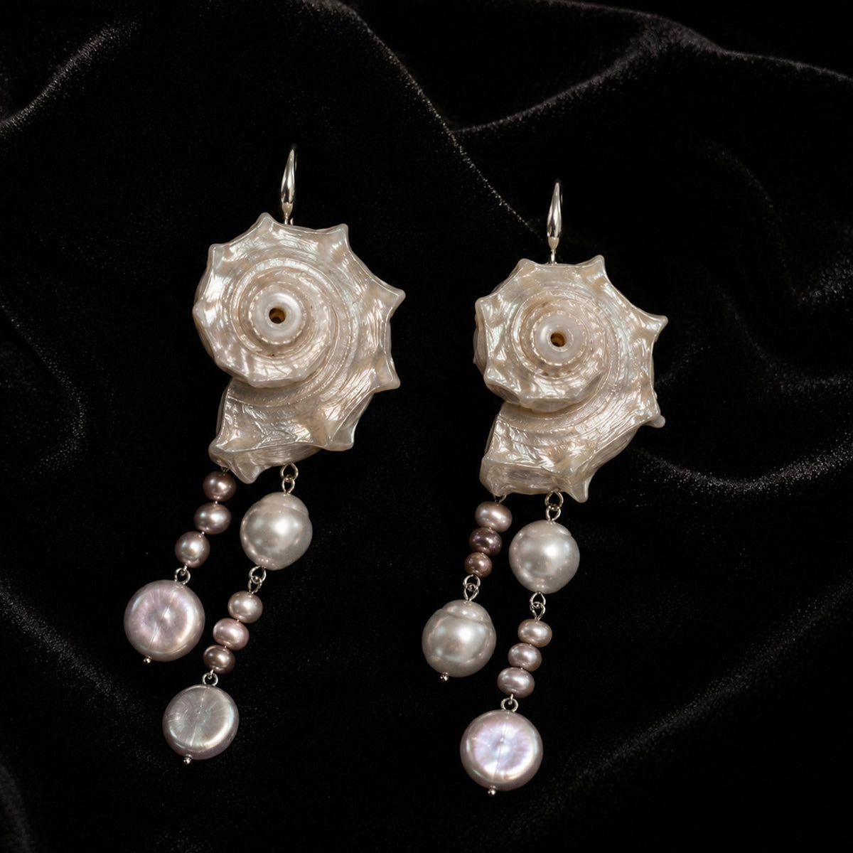 Spiral conch-shell earrings with several hanging pale bead strands displayed on black velvet.