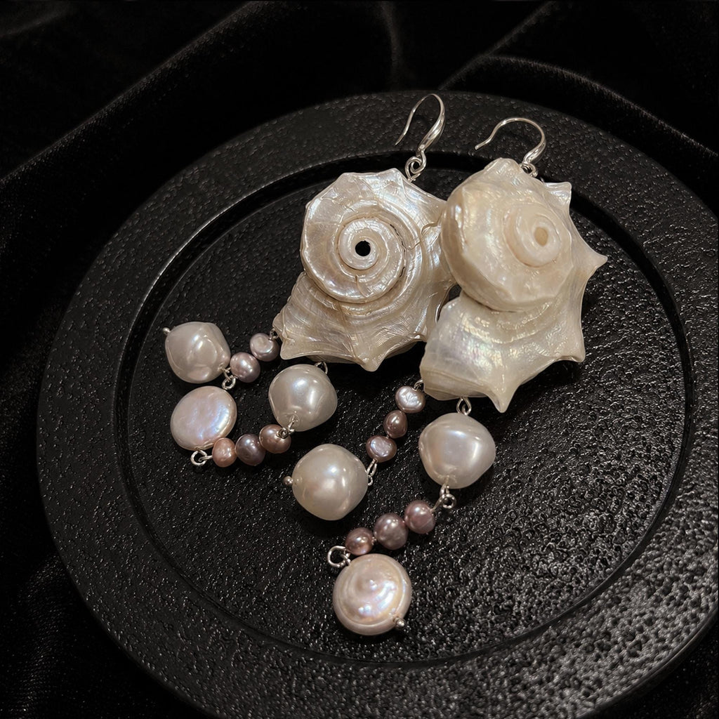 Spiral conch-shell earrings with pale and pink-toned bead drops on a round display stand.
