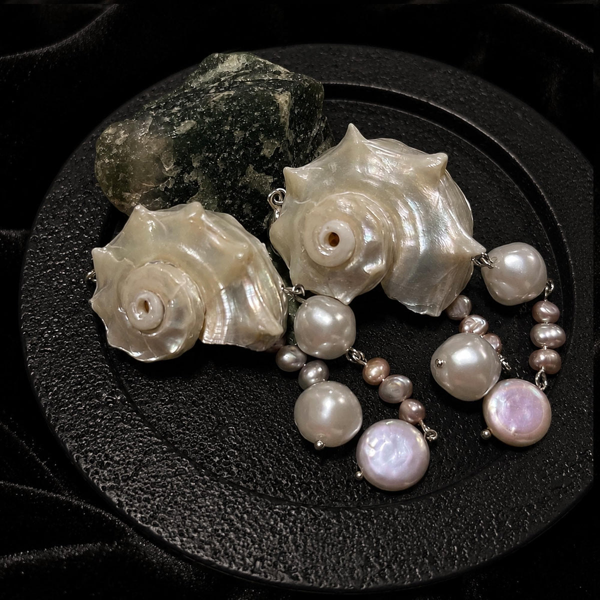 Two spiral conch-shell earrings with multiple bead drops arranged on a round black display.