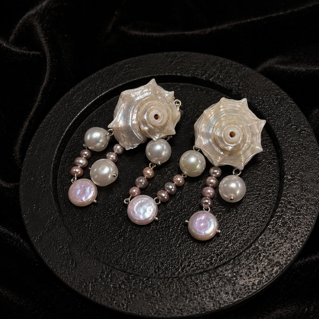 Pair of spiral conch-shell earrings with pale bead drops shown from above on a dark display.