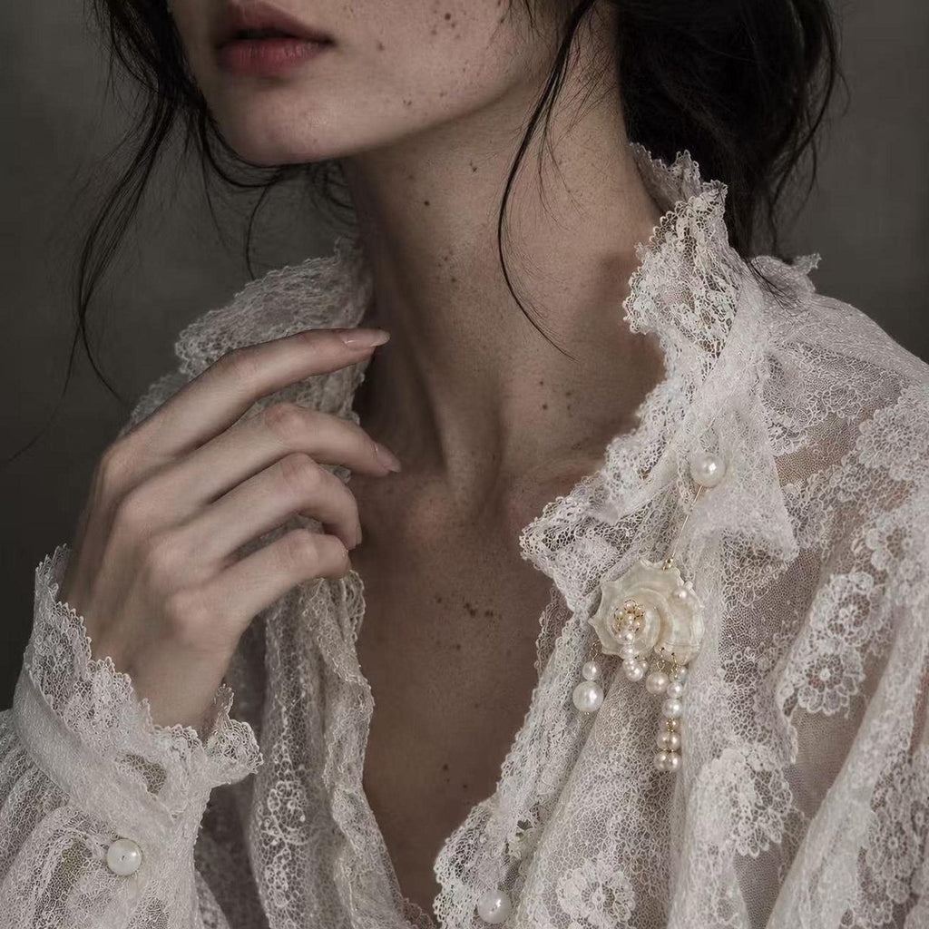 Conch-shell brooch with hanging pale beads pinned to an ivory lace garment.