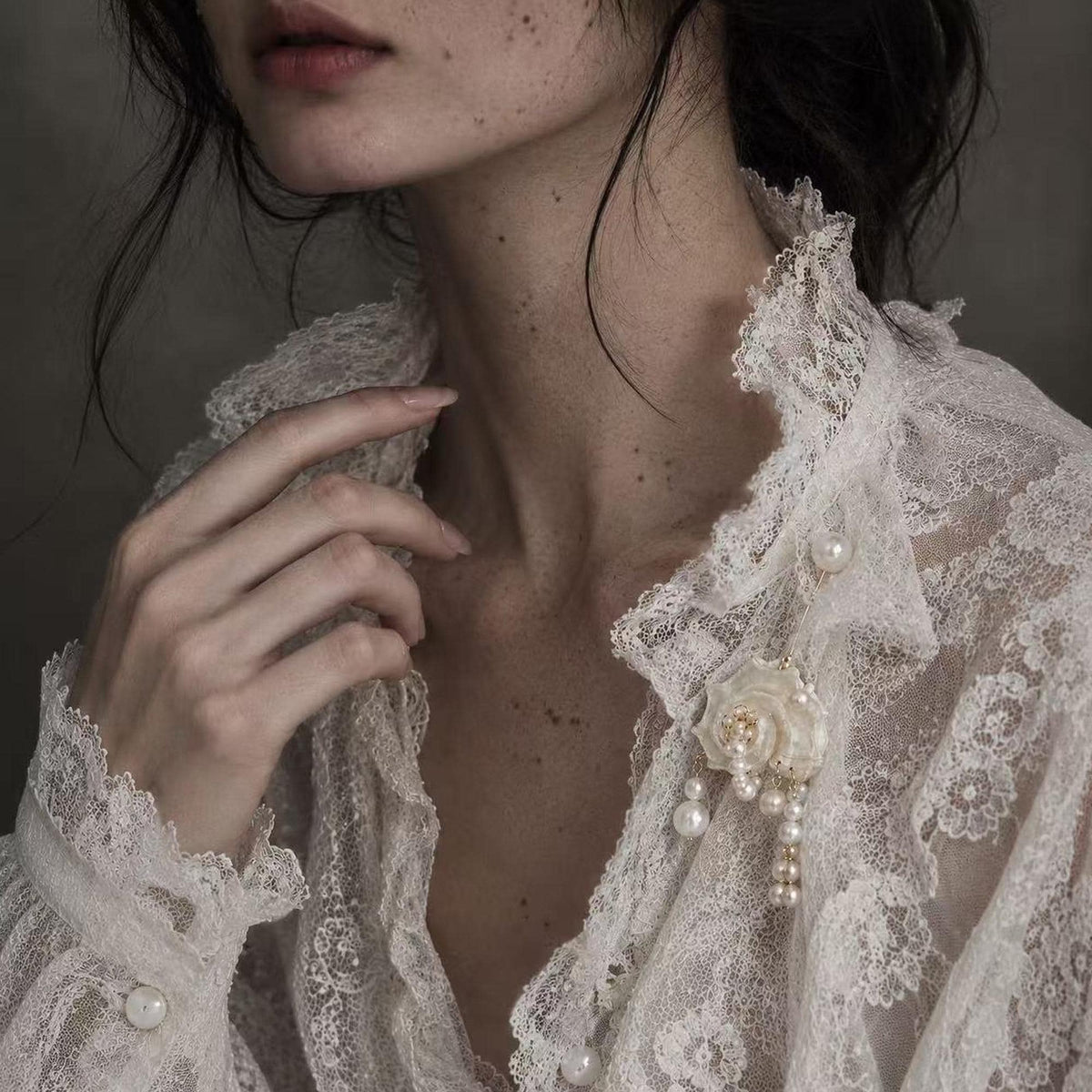 Conch-shell brooch with hanging pale beads pinned to an ivory lace garment.