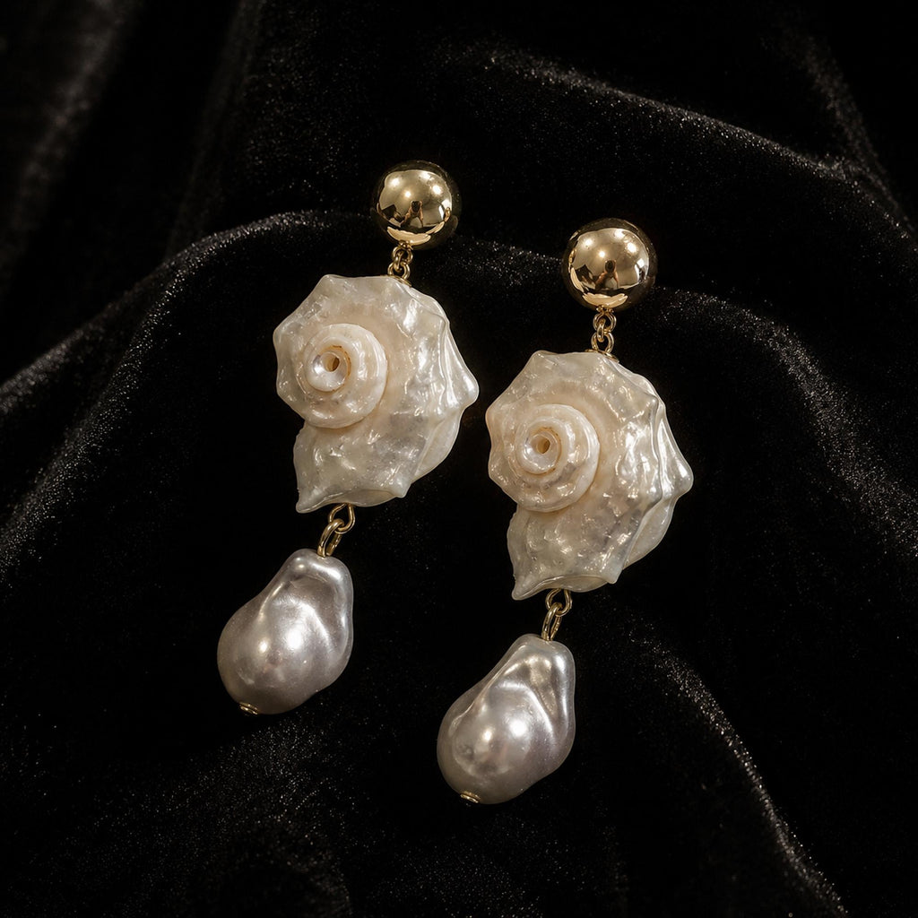 Pair of spiral conch-shell earrings with large pale teardrop beads on black velvet.