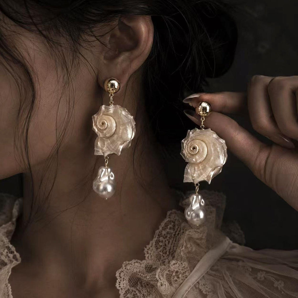 Spiral conch-shell earring shown worn while the second earring is held beside it.