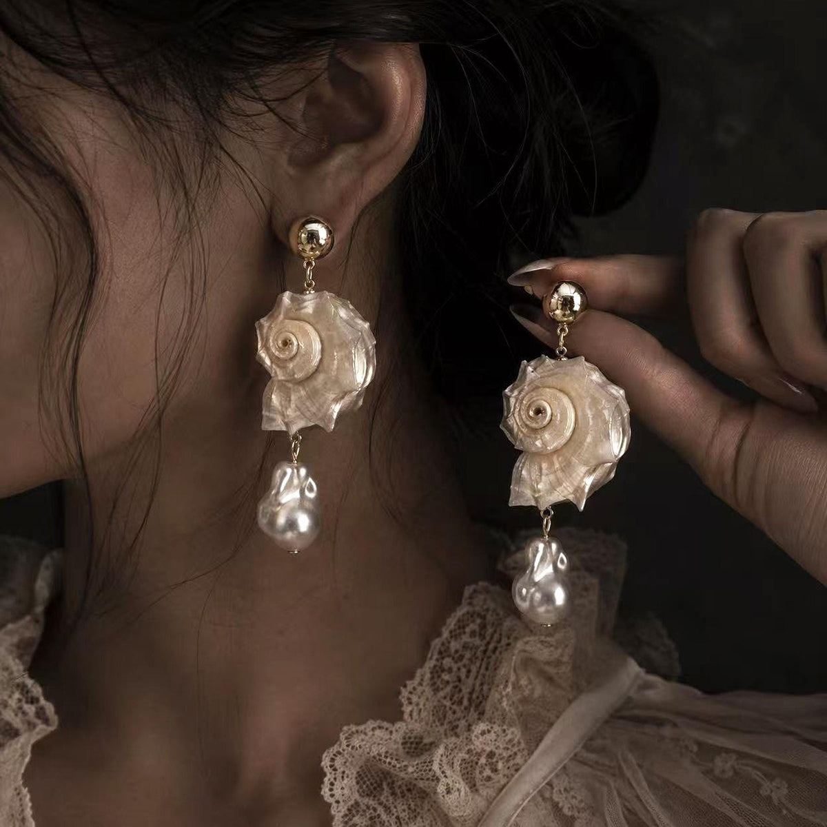 Spiral conch-shell earring shown worn while the second earring is held beside it.
