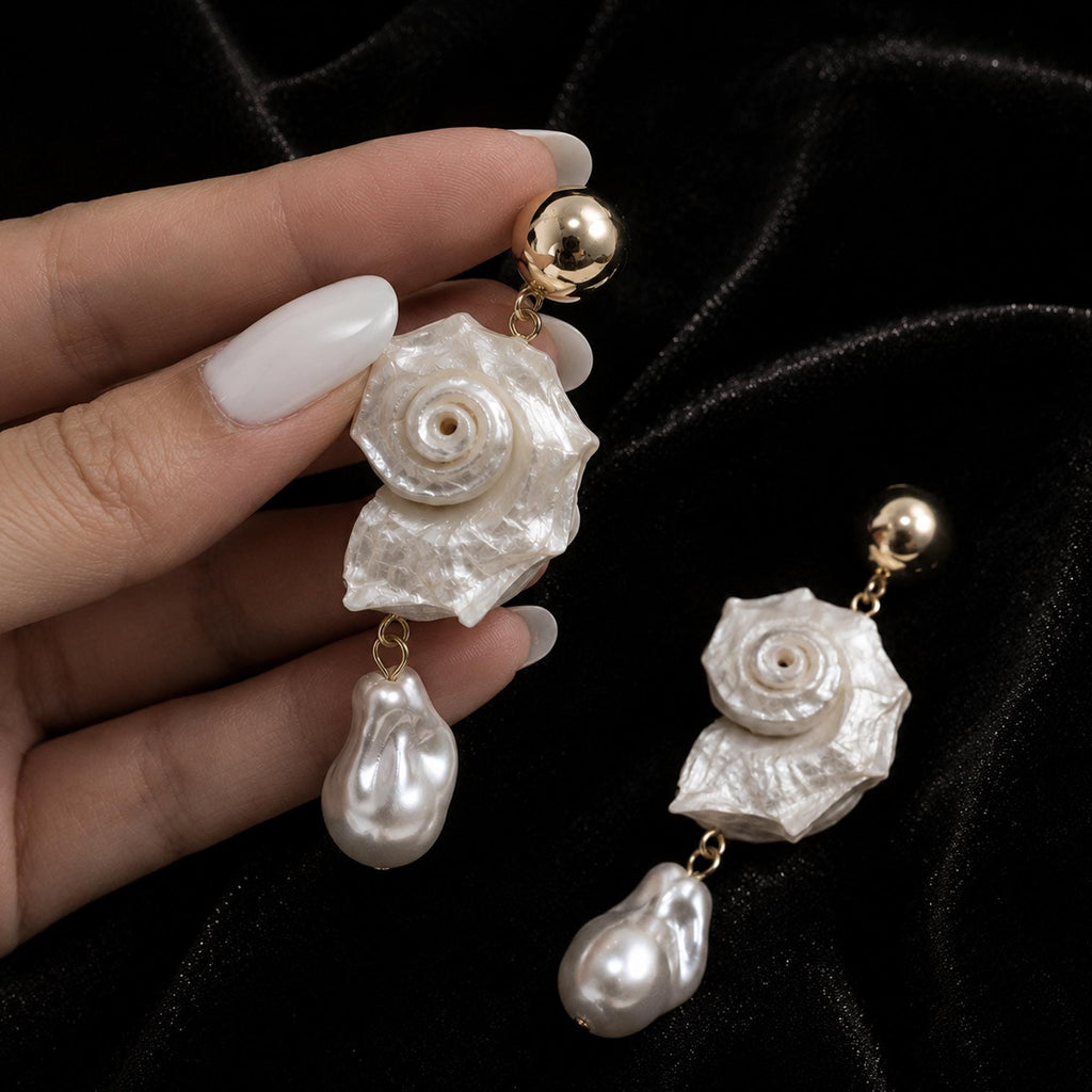 Pair of spiral conch-shell earrings with pale bead drops held in a hand.