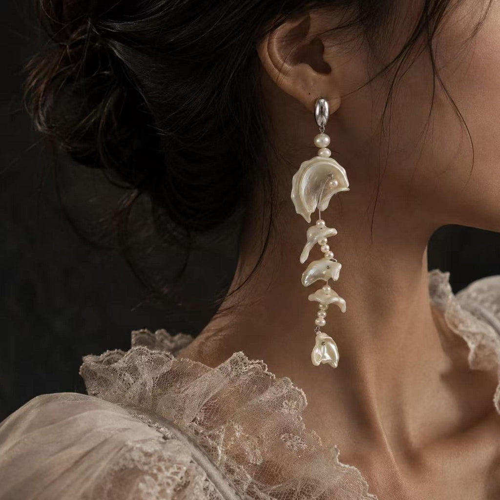 Shell-fragment drop earring with pale wavy sections and small connecting beads shown worn.