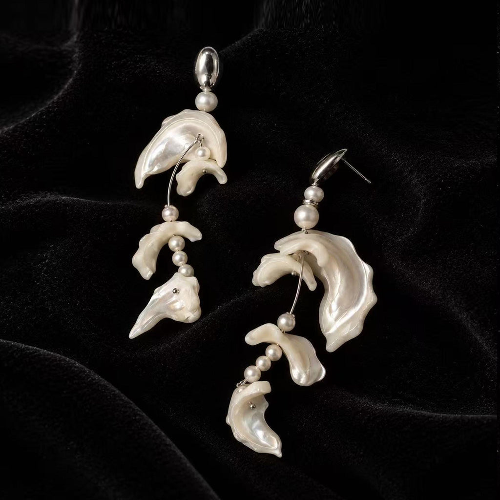 Pair of asymmetric shell-fragment drop earrings with pale wavy pieces on black velvet.