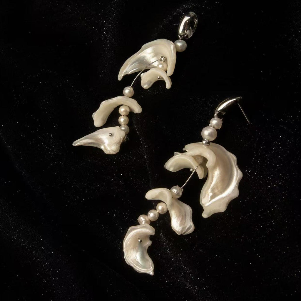 Close view of shell-fragment earrings showing their pale curved pieces and connecting beads.