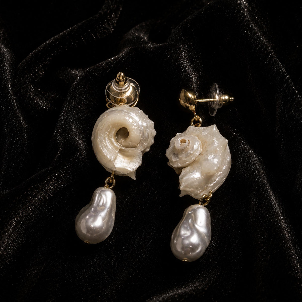 Rear view of spiral conch-shell earrings showing their stud posts and pale bead drops.