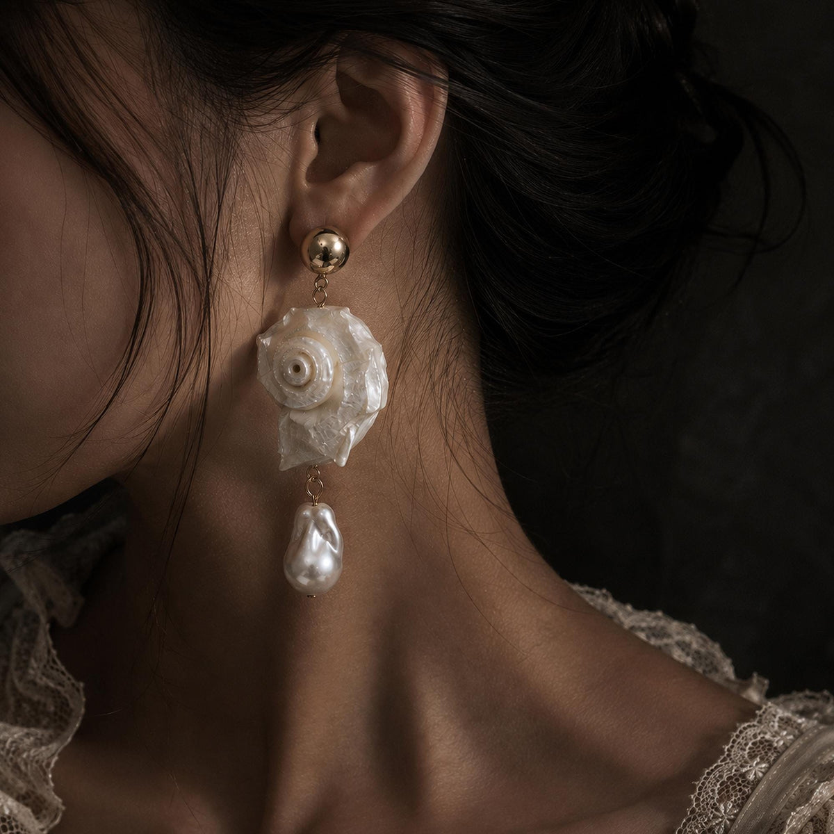 Spiral conch-shell earring with a large pale teardrop bead shown worn.