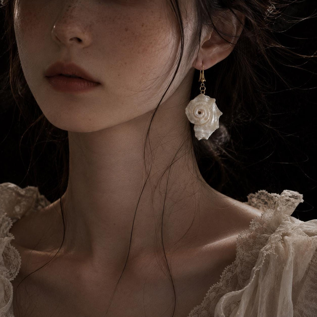 Conch-shell earring worn beside an ivory lace neckline.