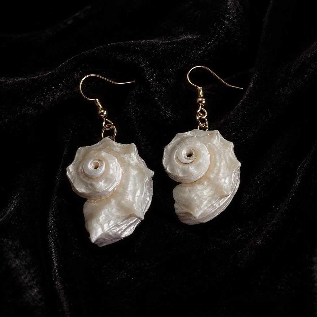 Pair of iridescent conch-shell earrings hanging from gold-tone hooks on black velvet.