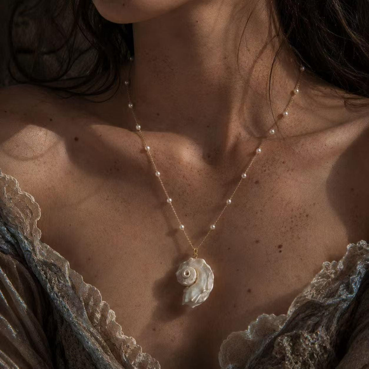 Iridescent conch-shell necklace worn above an ivory lace neckline.