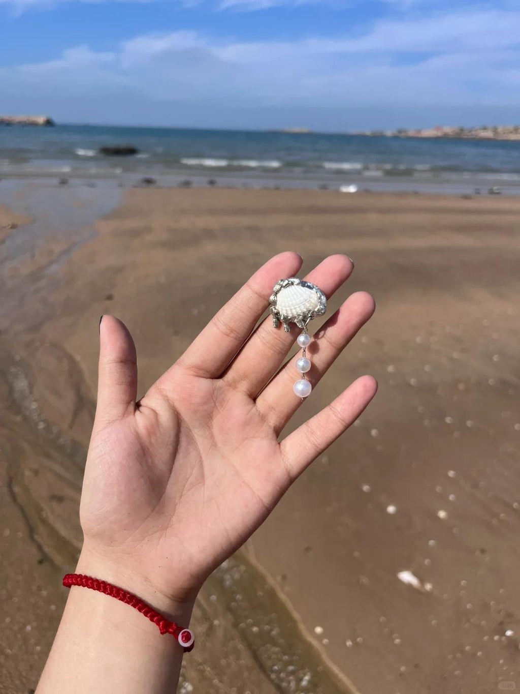 Shell Pearl Drop held across a palm beside the sea.