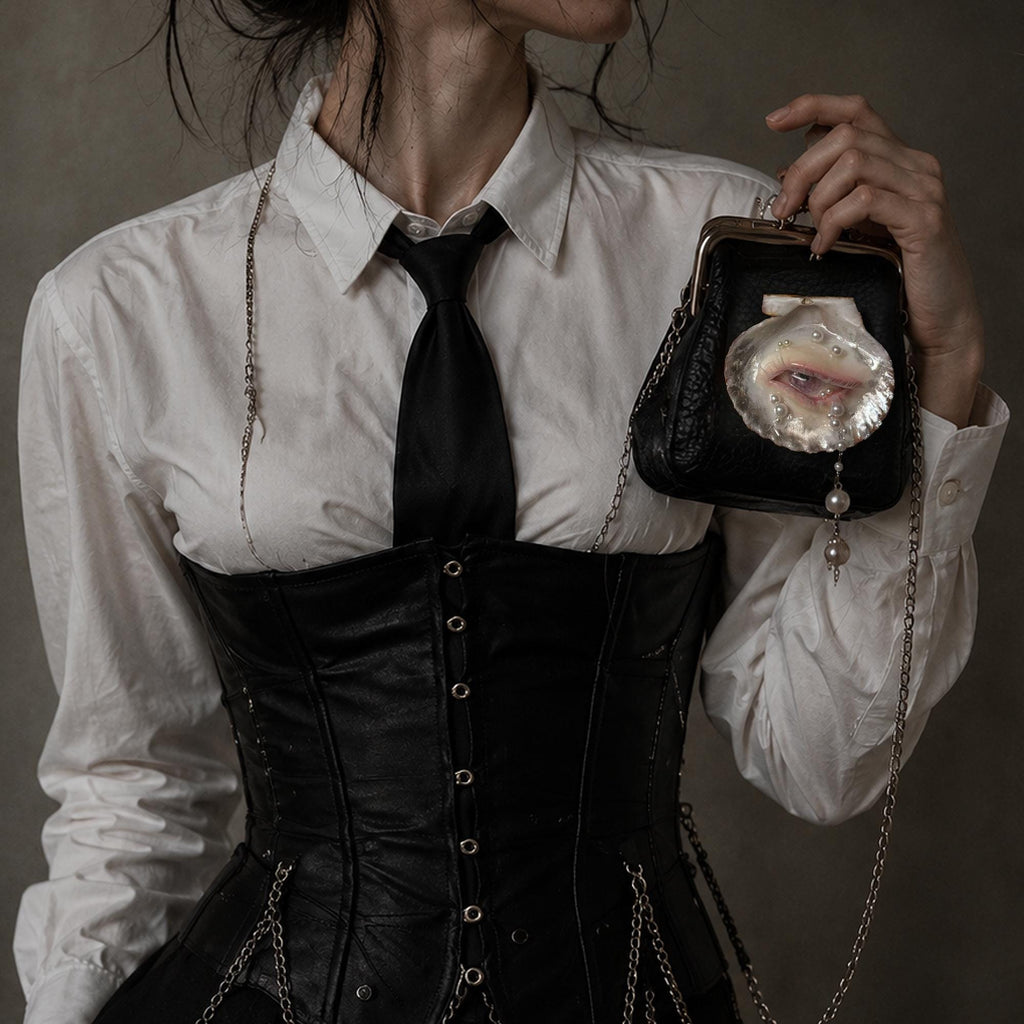 Oyster Eye Mini Crossbody Bag held beside a white shirt and black corset, showing the eye motif and chain.