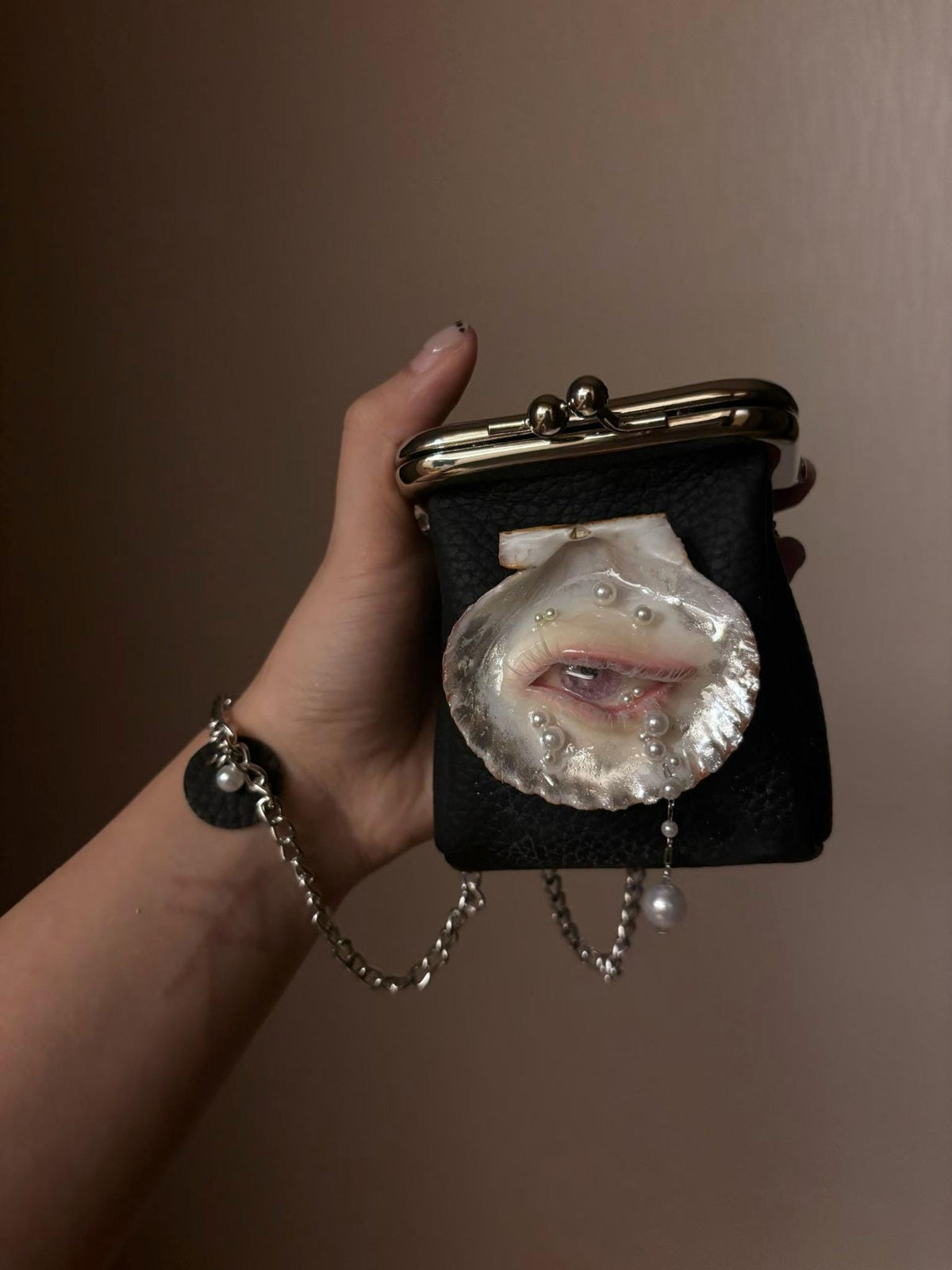 Oyster Eye Mini Crossbody Bag held in a hand to show its size and hanging pearl-like detail.