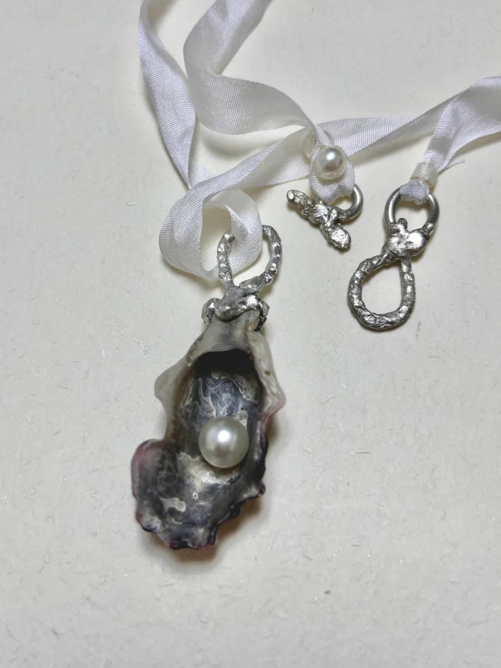 Shell Pearl Talisman pendant with ribbon and metal attachment components displayed beside it.
