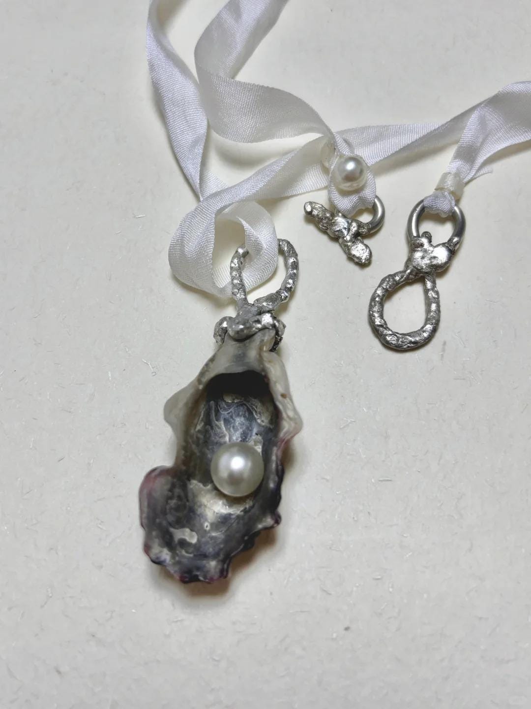 Shell Pearl Talisman pendant with ribbon and metal attachment components displayed beside it.