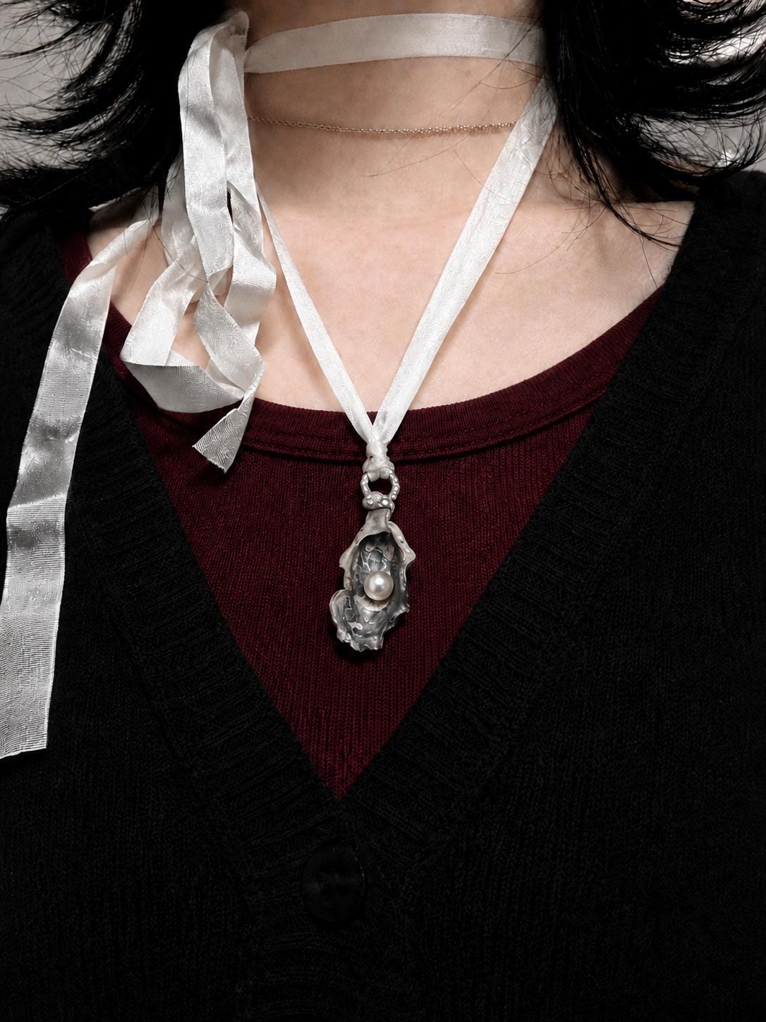 Shell Pearl Talisman pendant worn on ivory ribbon over a dark red top.