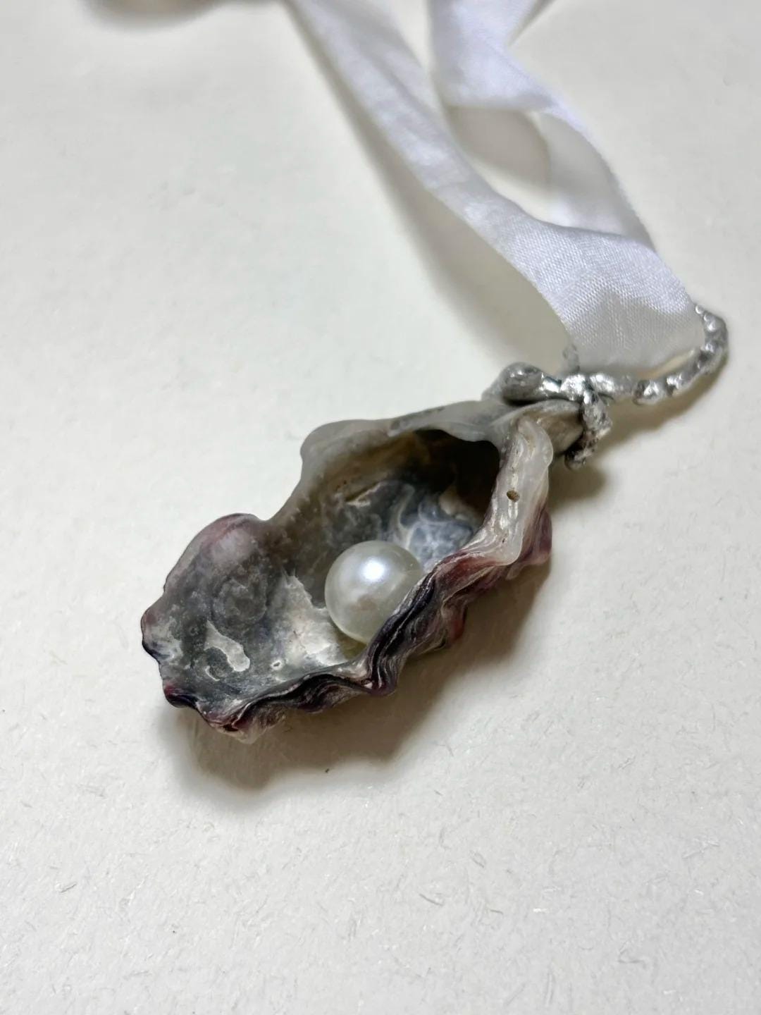 Angled view of the Shell Pearl Talisman pendant showing the dark shell interior and pale center.