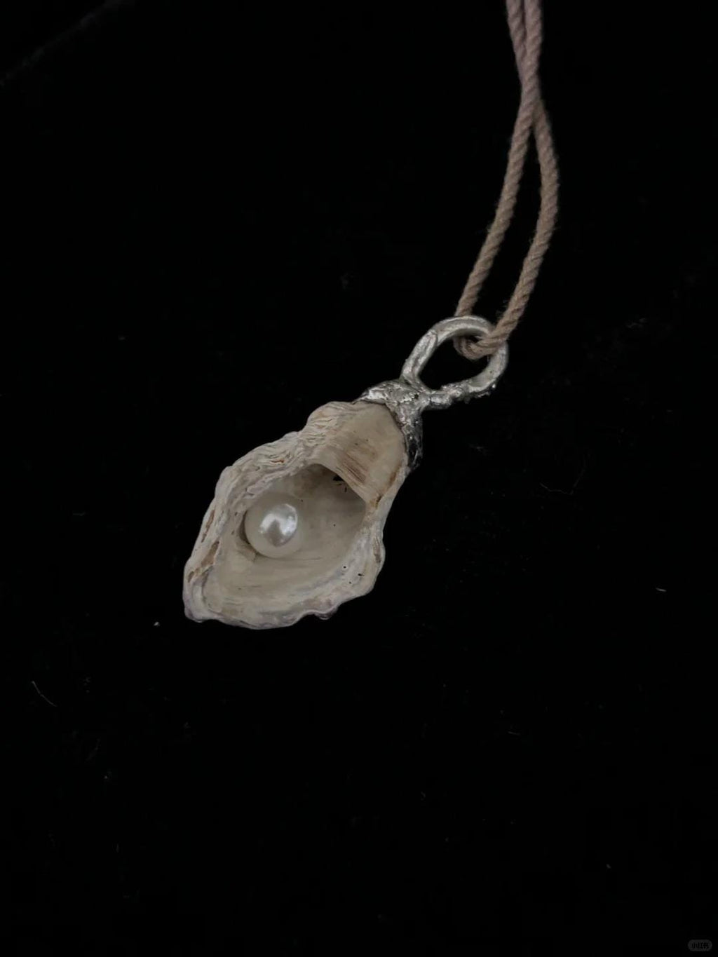 Shell Pearl Talisman pendant on brown cord against a dark background.