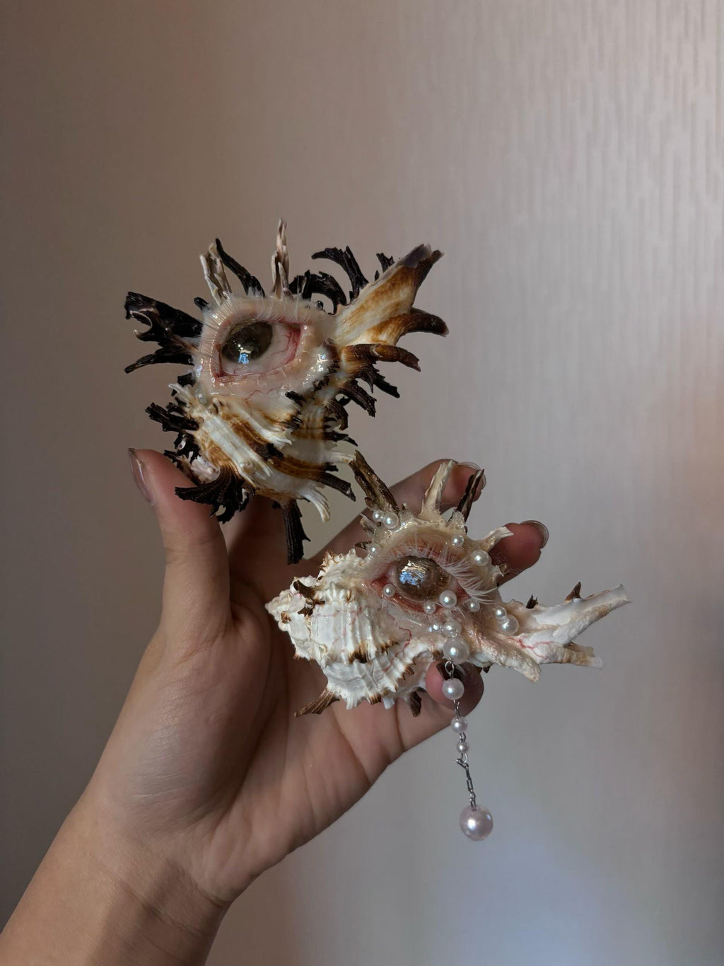 Two spiked shell-eye sculptures with dark and pale finishes held together for comparison.