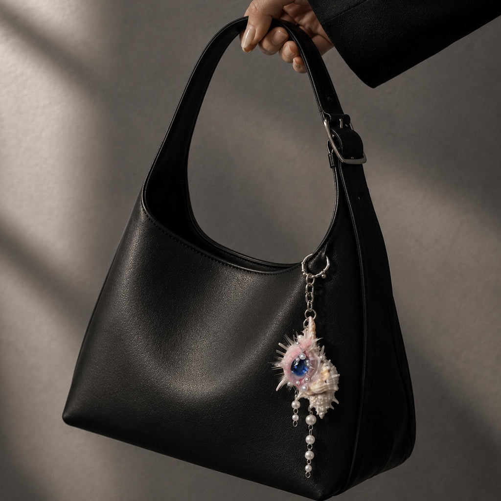 Conch Eye Talisman hanging as a charm from a black shoulder bag.