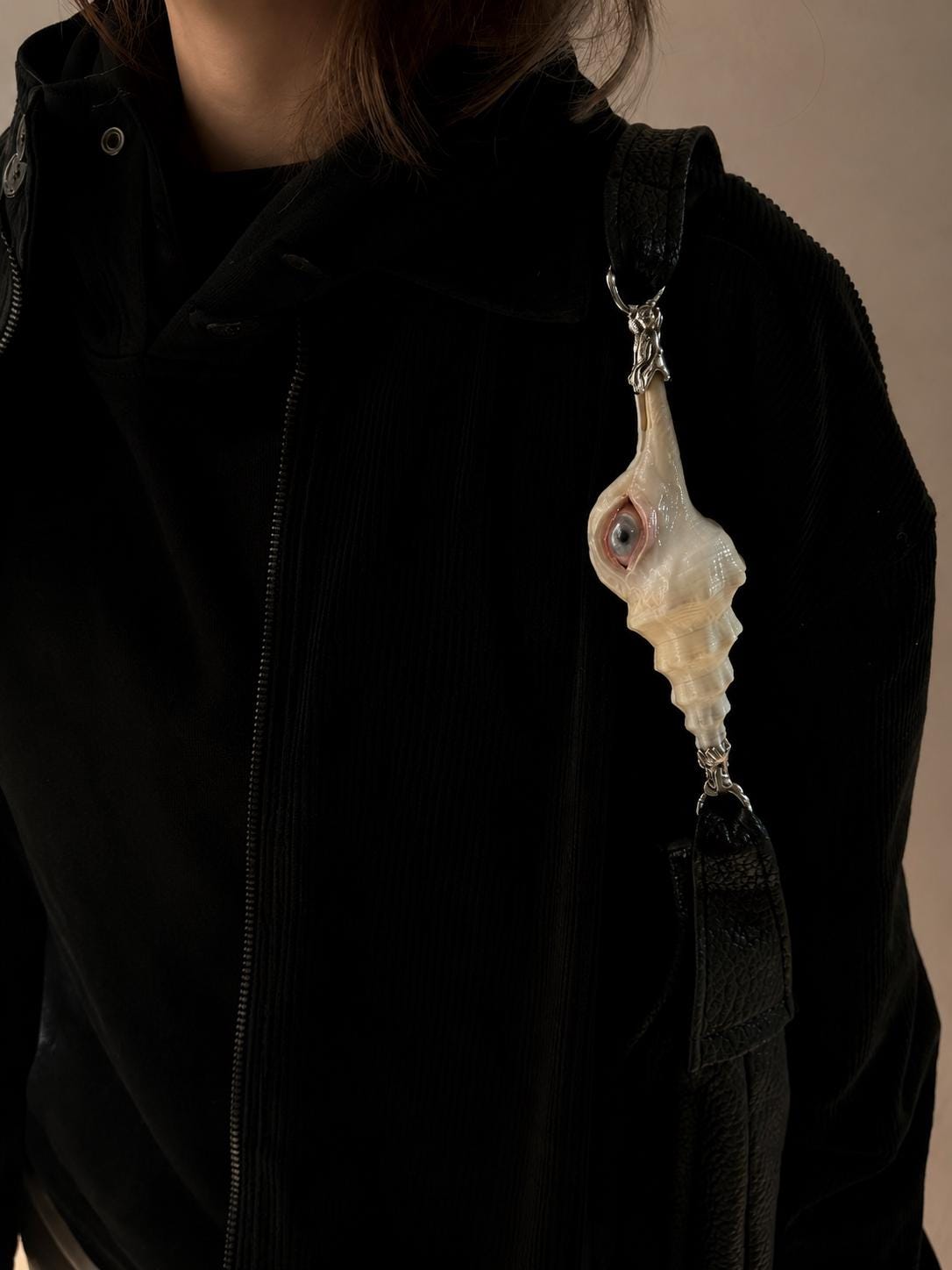 Close view of the Long Conch Eye Shoulder Bag strap and shell-eye ornament against a black outfit.