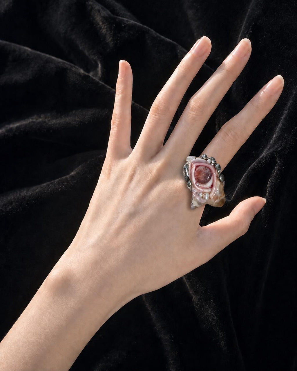 Shell-eye statement ring worn on an outstretched hand against black fabric.