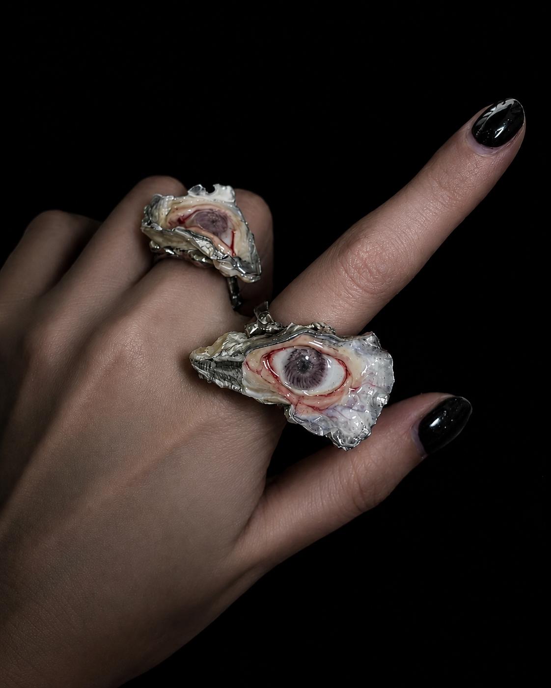 Two shell-eye statement rings with different eye colors worn together on a hand.