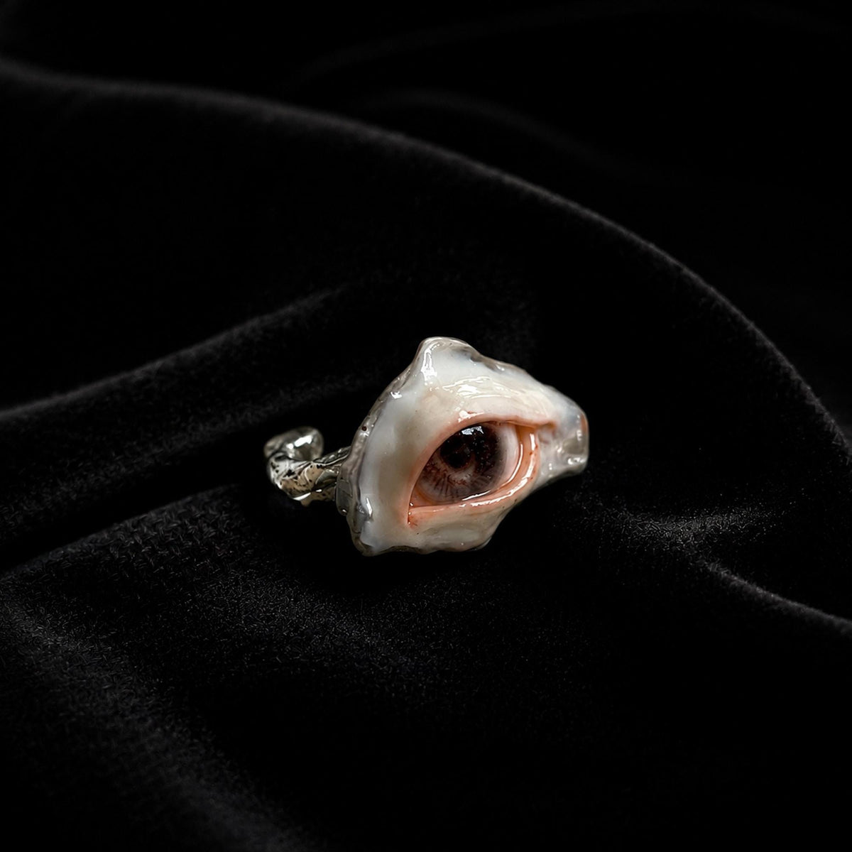 Brown-pupil oyster-eye ring resting at an angle on black velvet.
