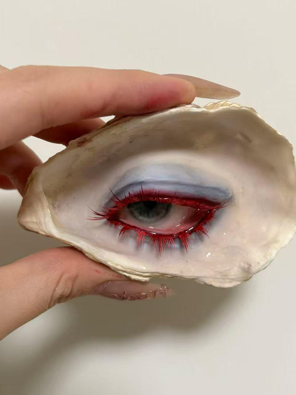 Angled hand-held view of Red-Lash Oyster Eye with red lashes and a pale iris.