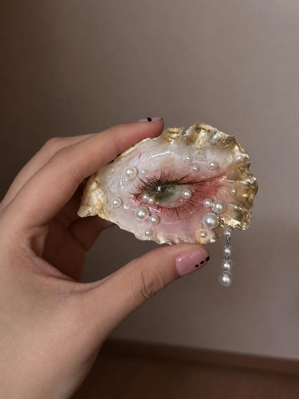Close-up of Gilded Oyster Eye held in a hand, showing the green iris and gold-toned shell edge.