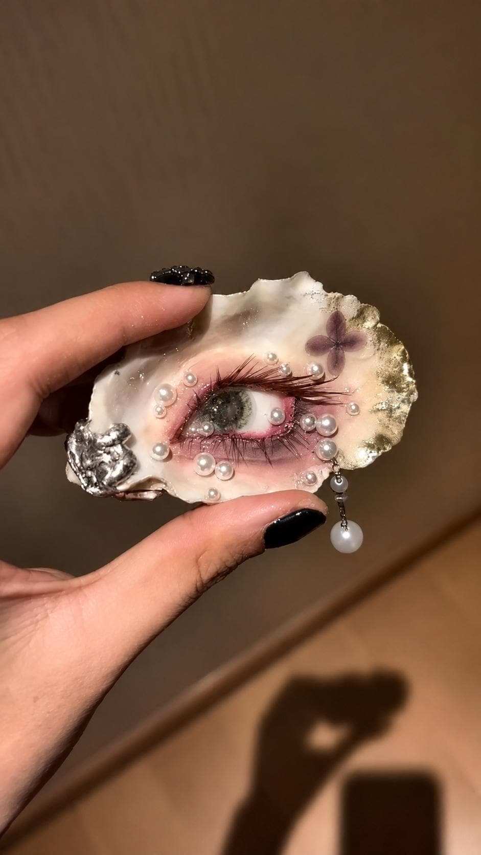 Gilded Oyster Eye held in sunlight, showing the pink eyelid and pearl-like decorations.