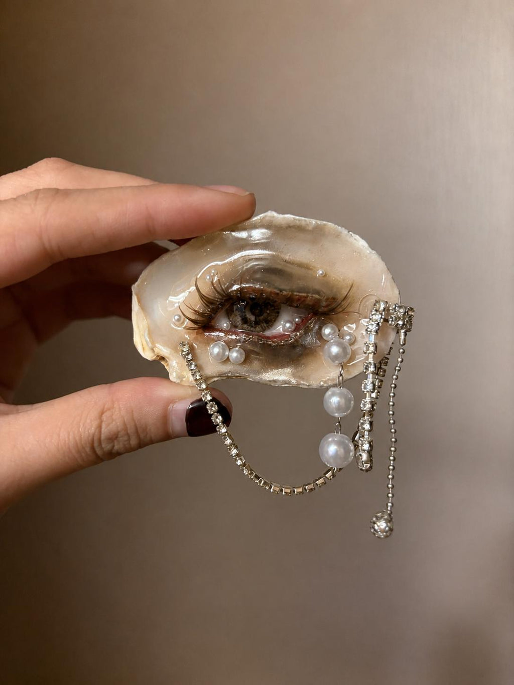 Brown Smoky Oyster Eye held against a light wall, showing smoky makeup and hanging chains.