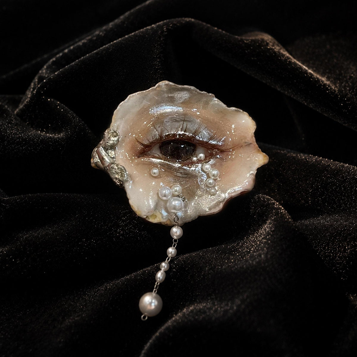 Brown Smoky Oyster Eye brooch with a hanging pearl-like drop shown on black velvet.
