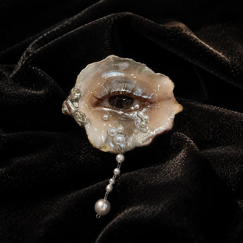 Brown Smoky Oyster Eye brooch with a hanging pearl-like drop shown on black velvet.