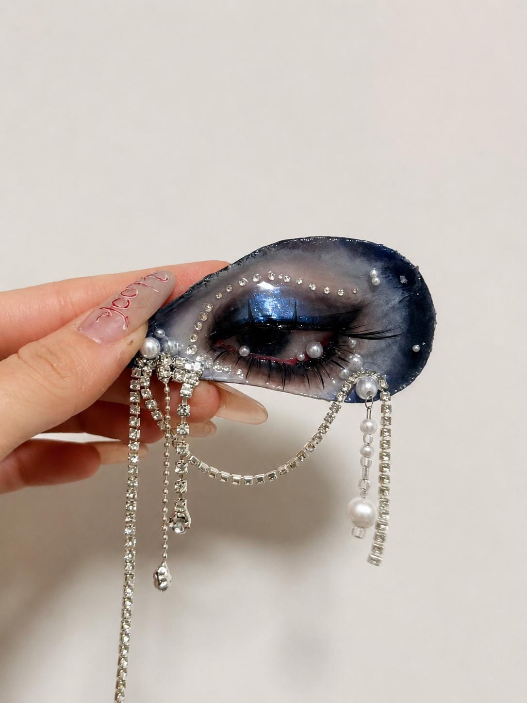 Blue Smoky Shell Eye held in a hand, showing the pale shell interior and dangling chains.