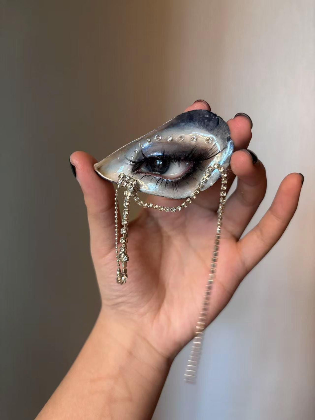 Blue Smoky Shell Eye held across a palm, showing blue makeup and hanging chains.