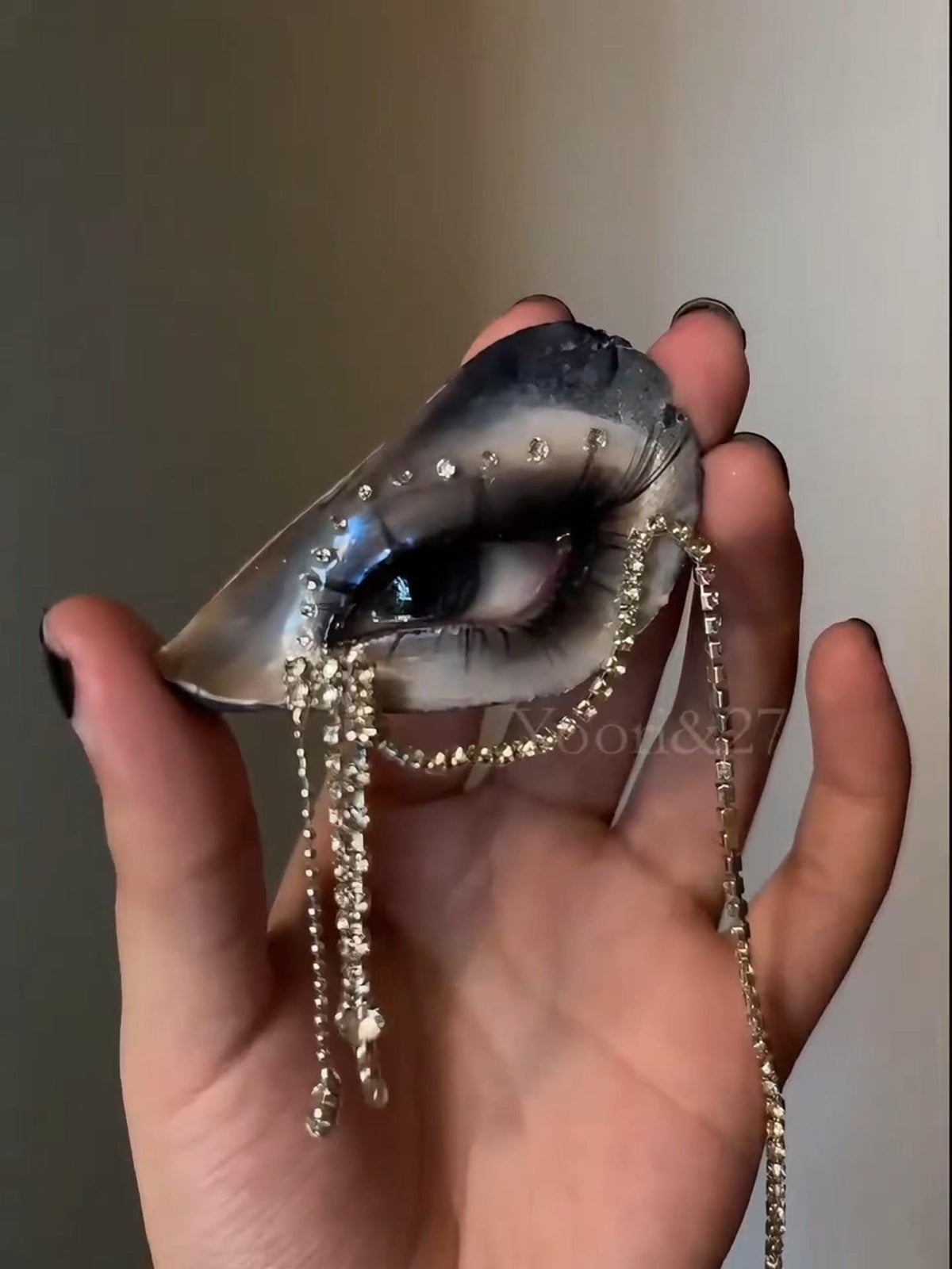 Angled hand-held view of Blue Smoky Shell Eye with draped bead chains.