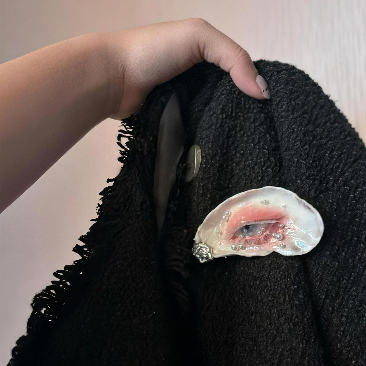 Blue-eye oyster-shell brooch shown pinned to a dark knitted garment held in a hand.
