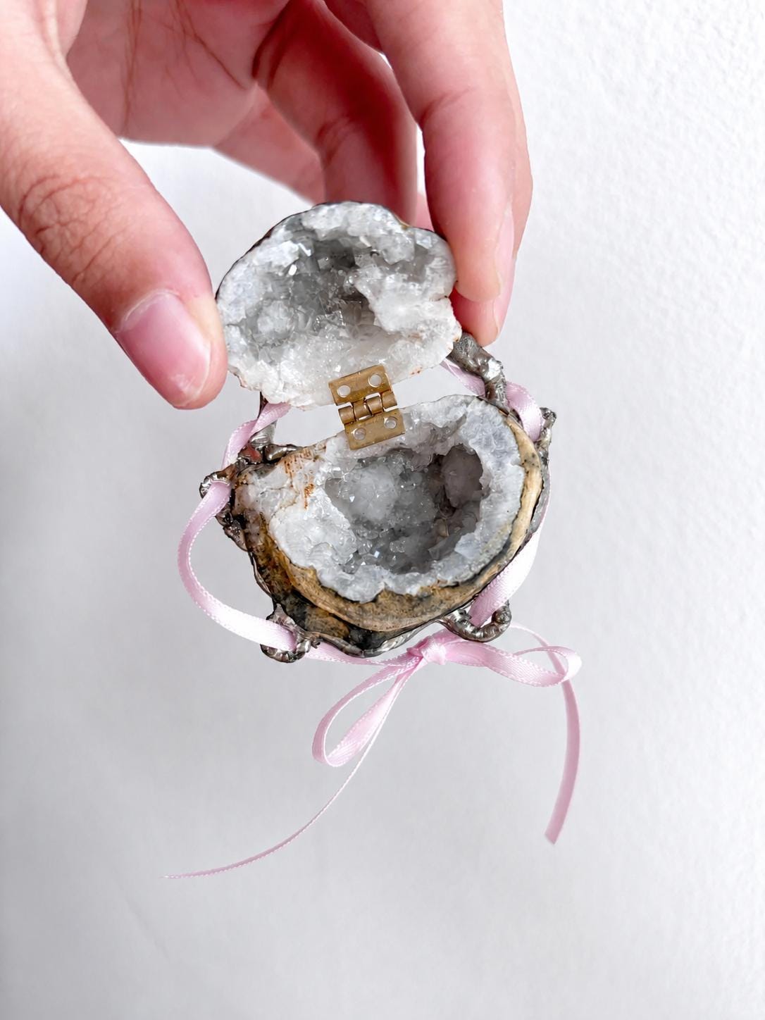 Open Geode Shell Trinket Box with grey crystal texture and pink ribbon, held against a light wall.