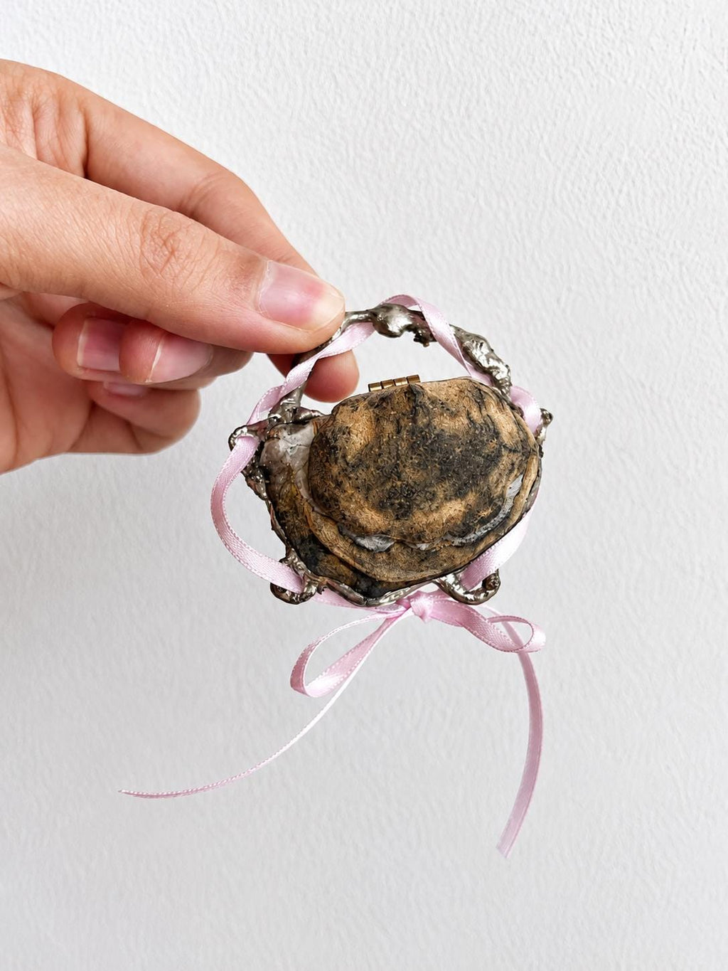 Reverse of a closed Geode Shell Trinket Box showing its dark gold-toned exterior and pink ribbon.