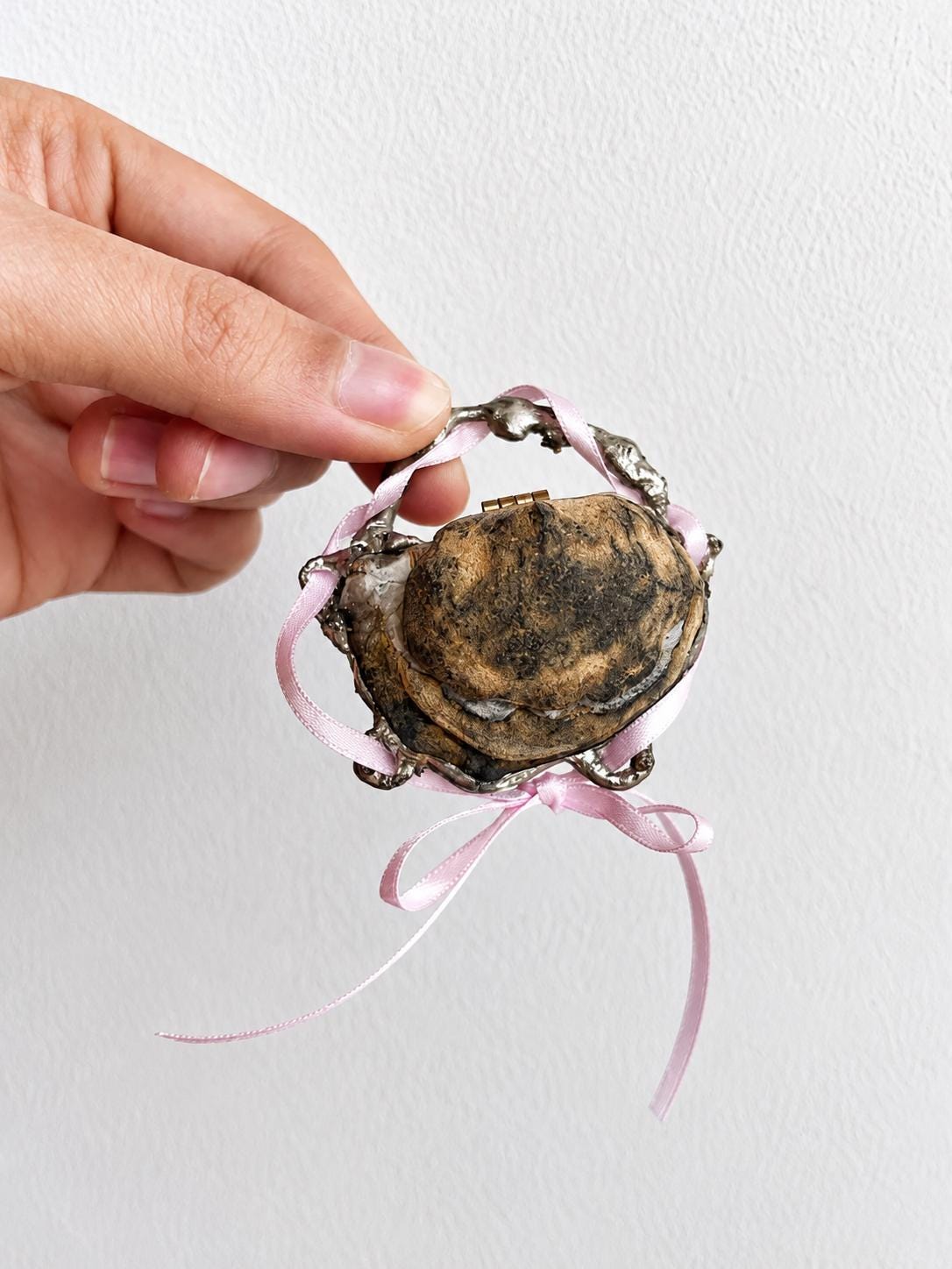 Reverse of a closed Geode Shell Trinket Box showing its dark gold-toned exterior and pink ribbon.