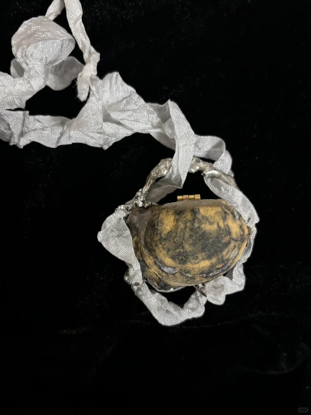 Closed Geode Shell Trinket Box with pale ribbon, resting on black velvet.